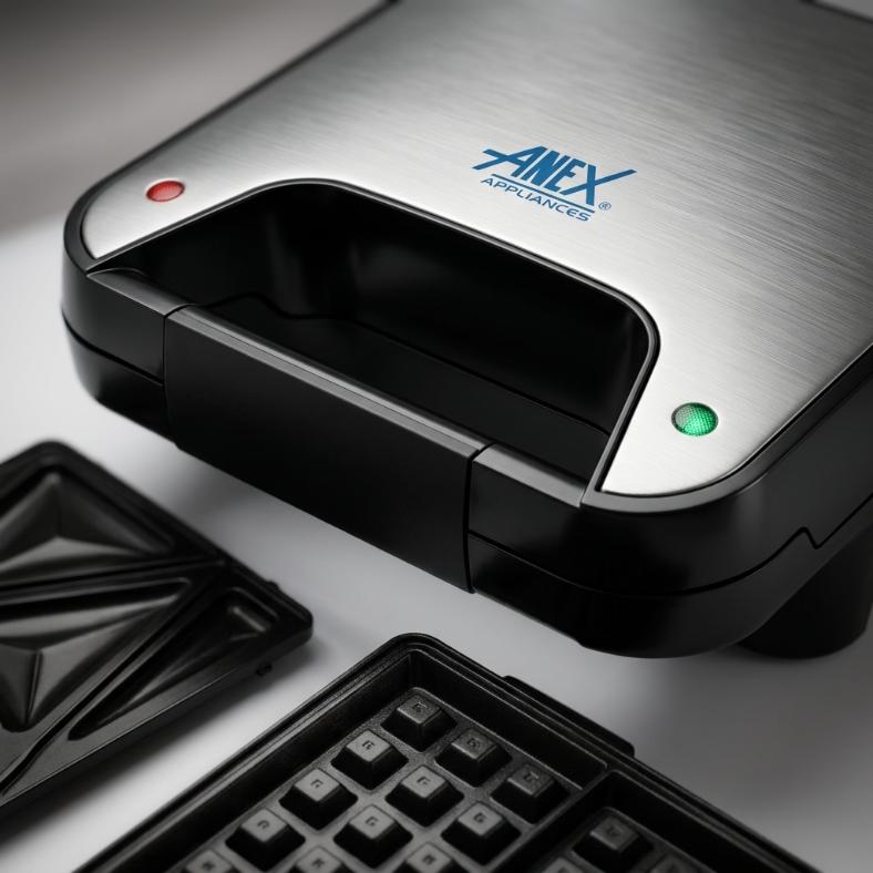 Anex Appliances stainless steel and black sandwich maker shown closed with the lid featuring the blue Anex Appliances logo, alongside open waffle plates in the foreground on a light gray surface. 
Anex AG-2047 Deluxe Sandwich Maker
