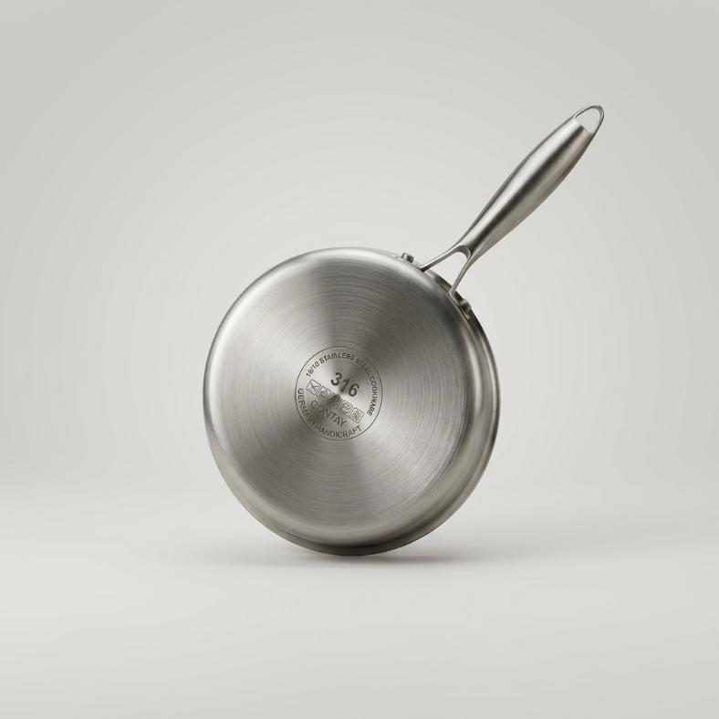 Studio shot of a stainless steel honeycomb milk pan with a tempered glass lid and ergonomic handle on a white background.
